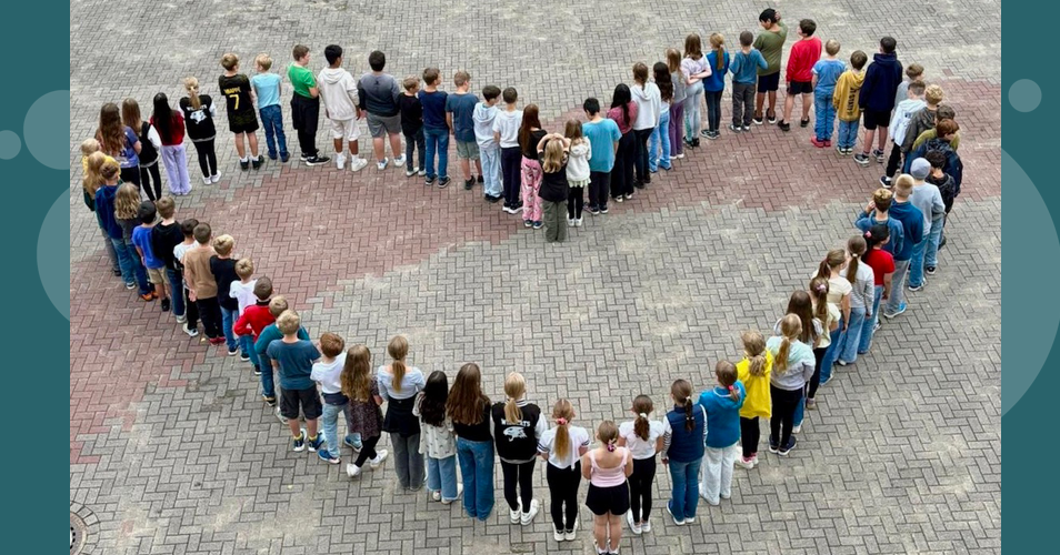 Kinder stehen in Herzform auf dem Schulhof
